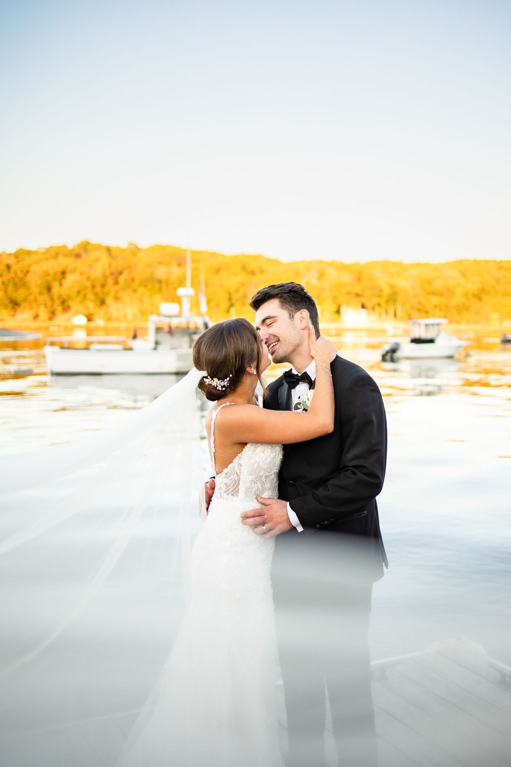 A romantic wedding portrait at sunset by a marina with boats in the background.