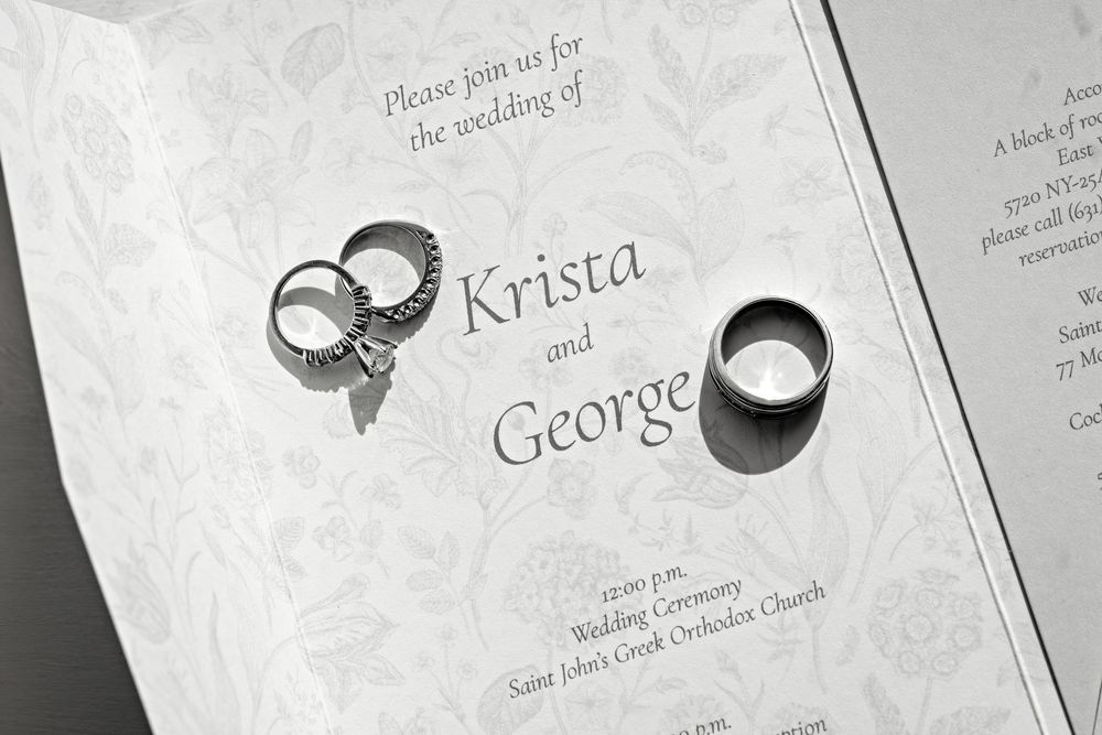 Wedding invitation for Krista and George with two silver rings on elegant white embossed stationery.