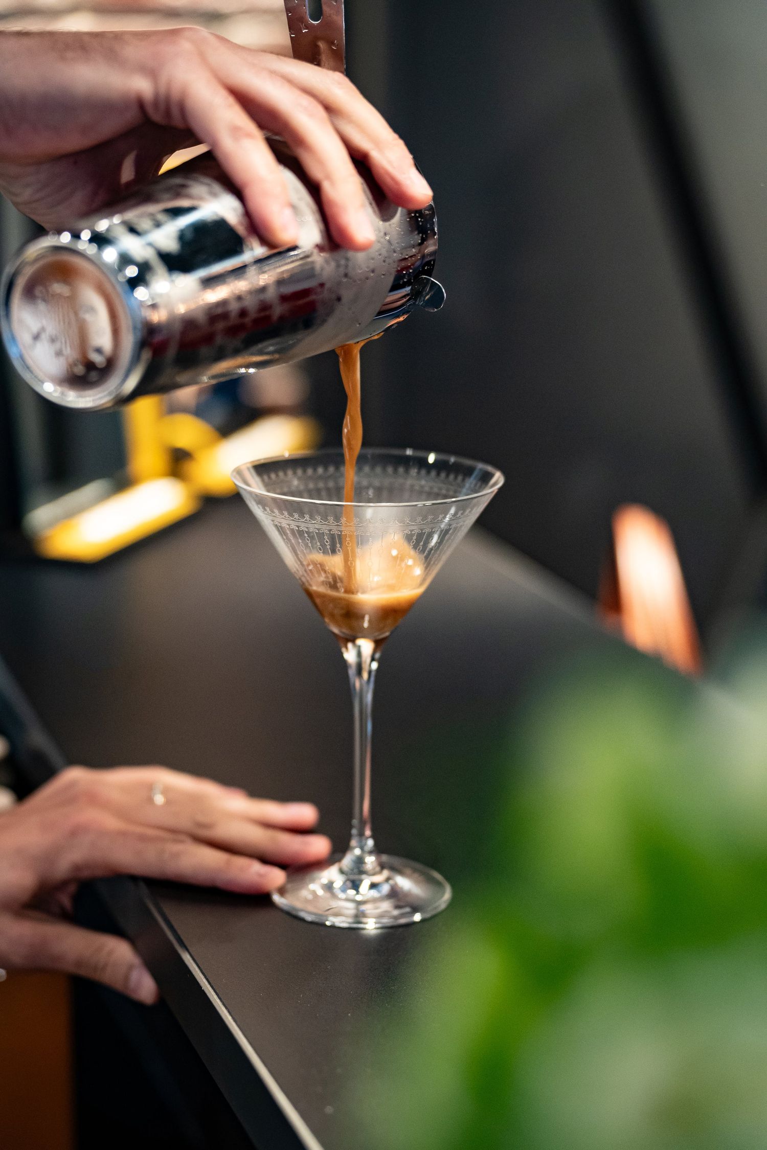 Bartender pouring an espresso martini cocktail from a shaker into a martini glass.