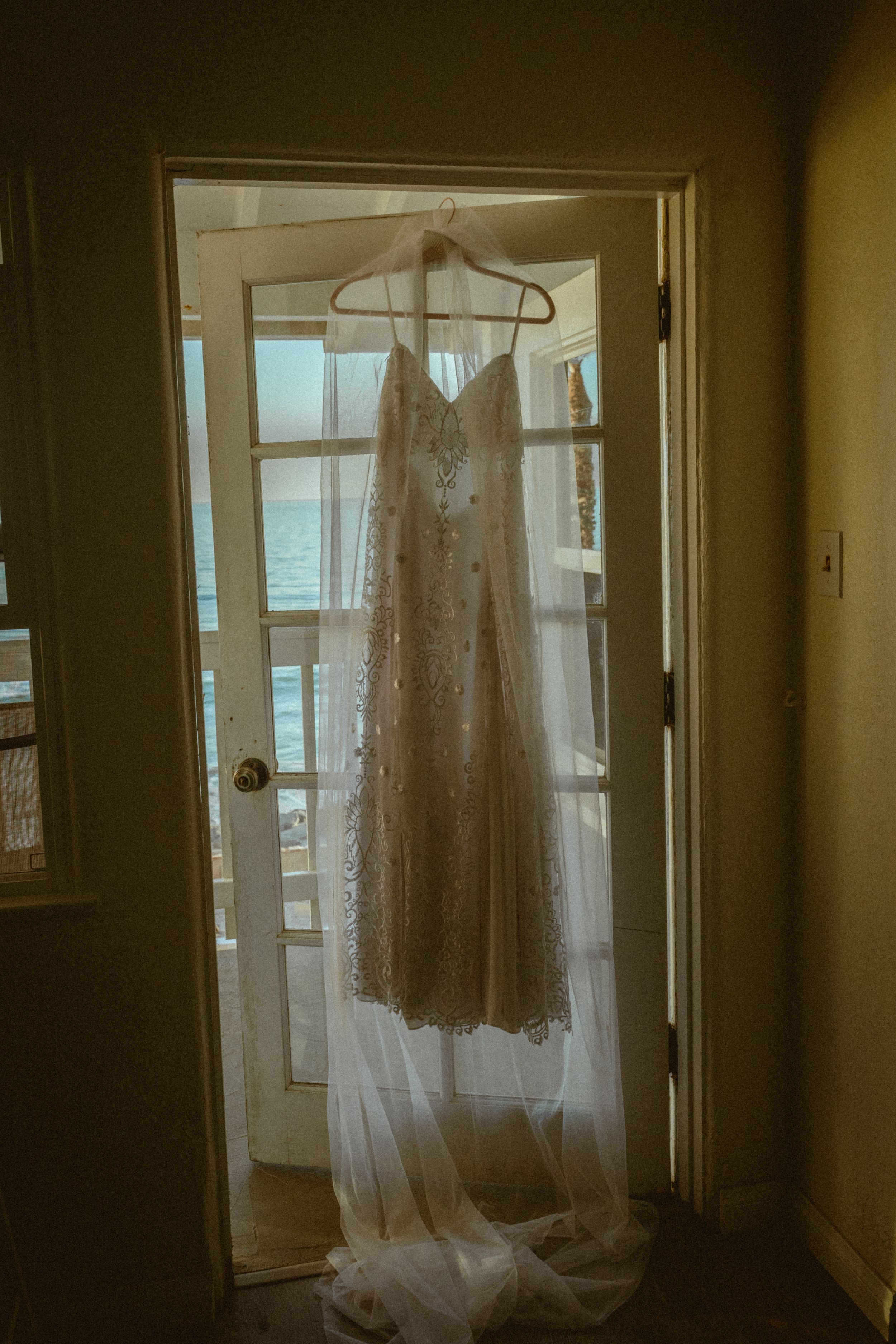 Wedding dress hanging in window creating ethereal silhouette in warm natural light.