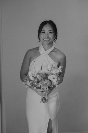 Bride in elegant white halter dress holding beautiful floral bouquet during photo session.