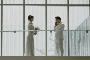 A couple in wedding attire poses together on a balcony with white walls.