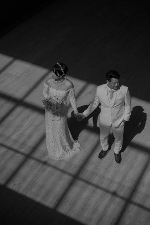 A black and white photo of newlyweds standing in dramatic window light.