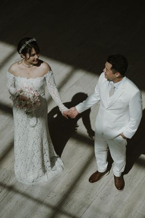 Artistic overhead view of bride and groom standing together on light wooden floor in white wedding attire.