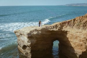 A dramatic coastal scene with a natural rock arch formation over blue ocean waters.