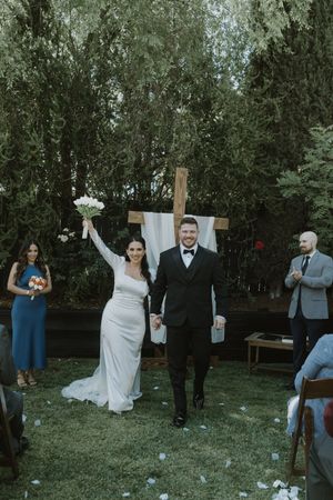 A couple celebrates at an outdoor garden wedding ceremony with wedding party members in blue dresses nearby.