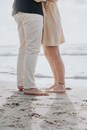 Close-up of two pairs of bare feet standing together on wet sand at the beach.