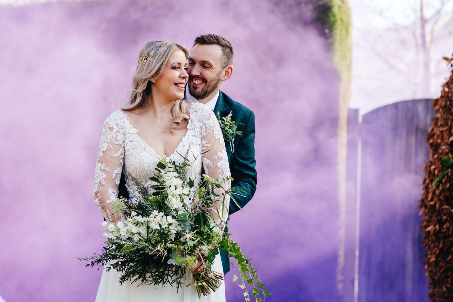 A joyful wedding portrait with purple smoke effects and a lush greenery bouquet.