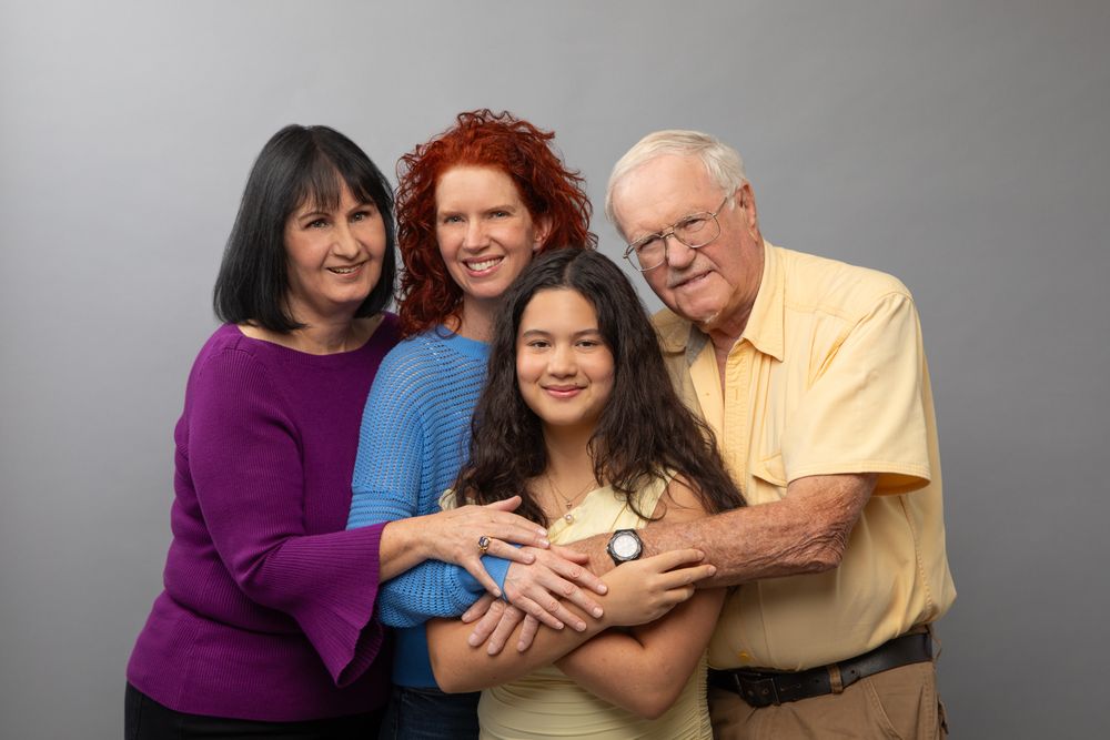 Multigenerational family portrait on gray background showing Grandma, Mother, Grandpa and Granddaughter