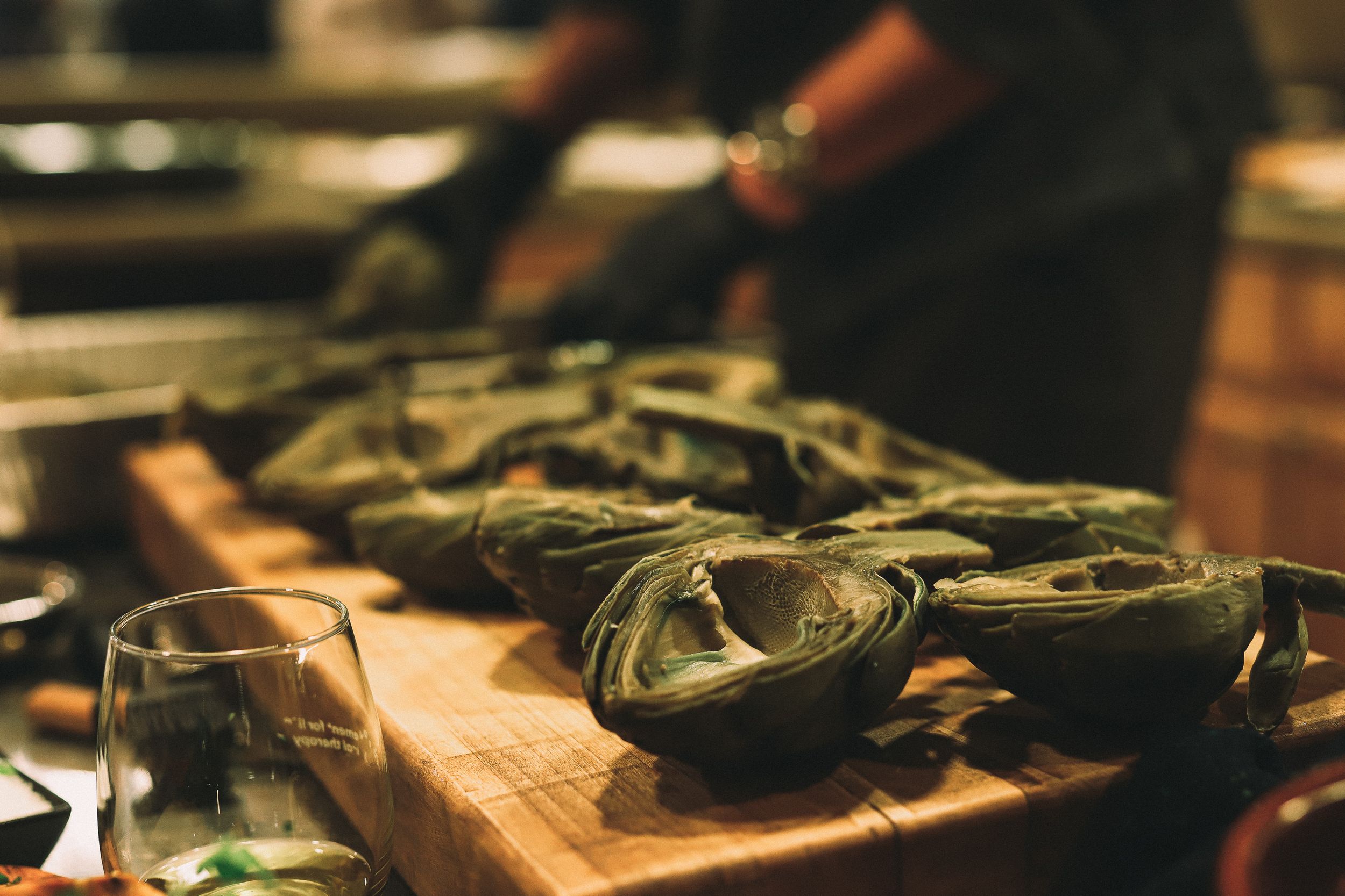 Fresh artichokes being prepared on a wooden cutting board in a rustic kitchen setting.