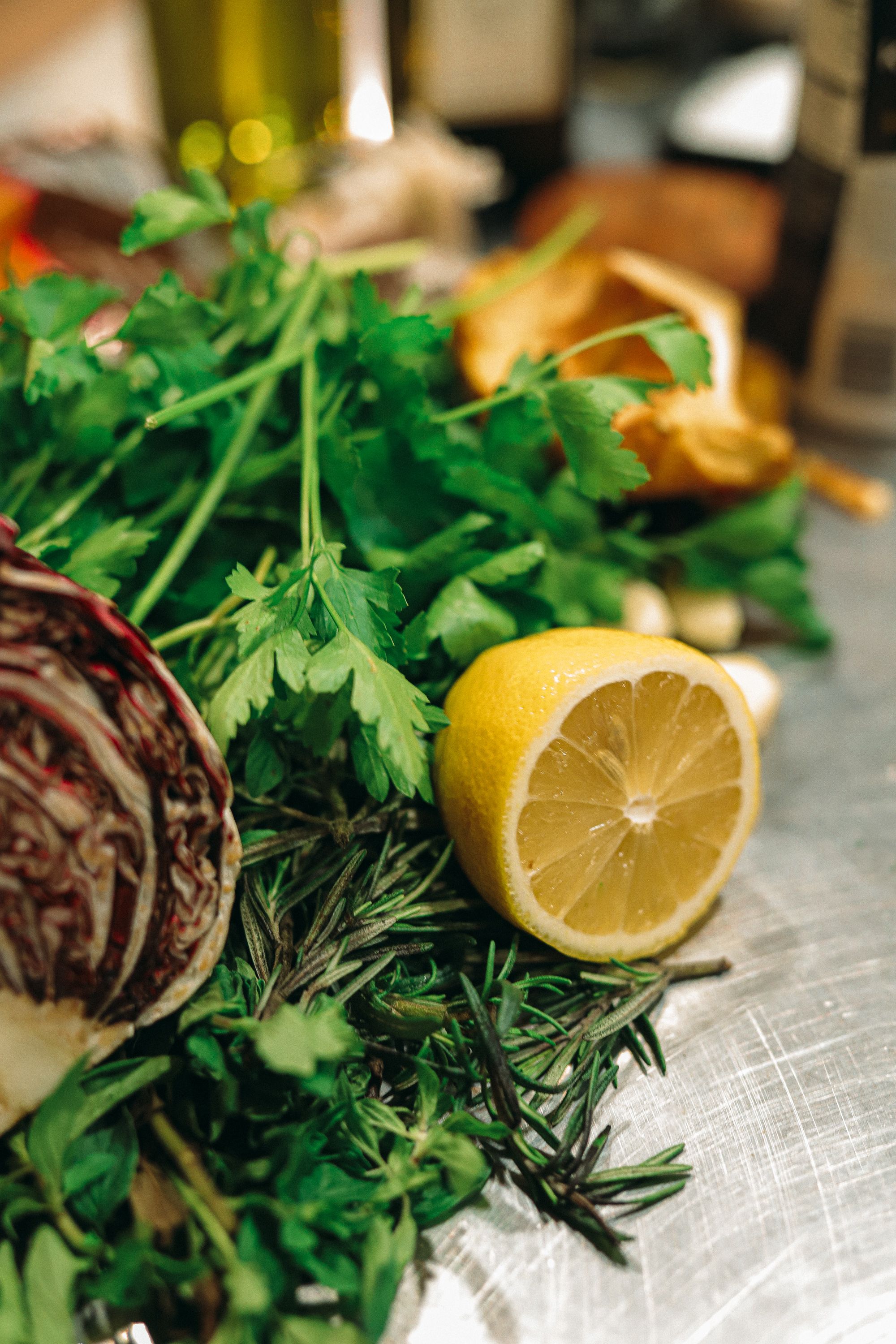 Fresh herbs, lemon, and radicchio arranged on a metal preparation surface.