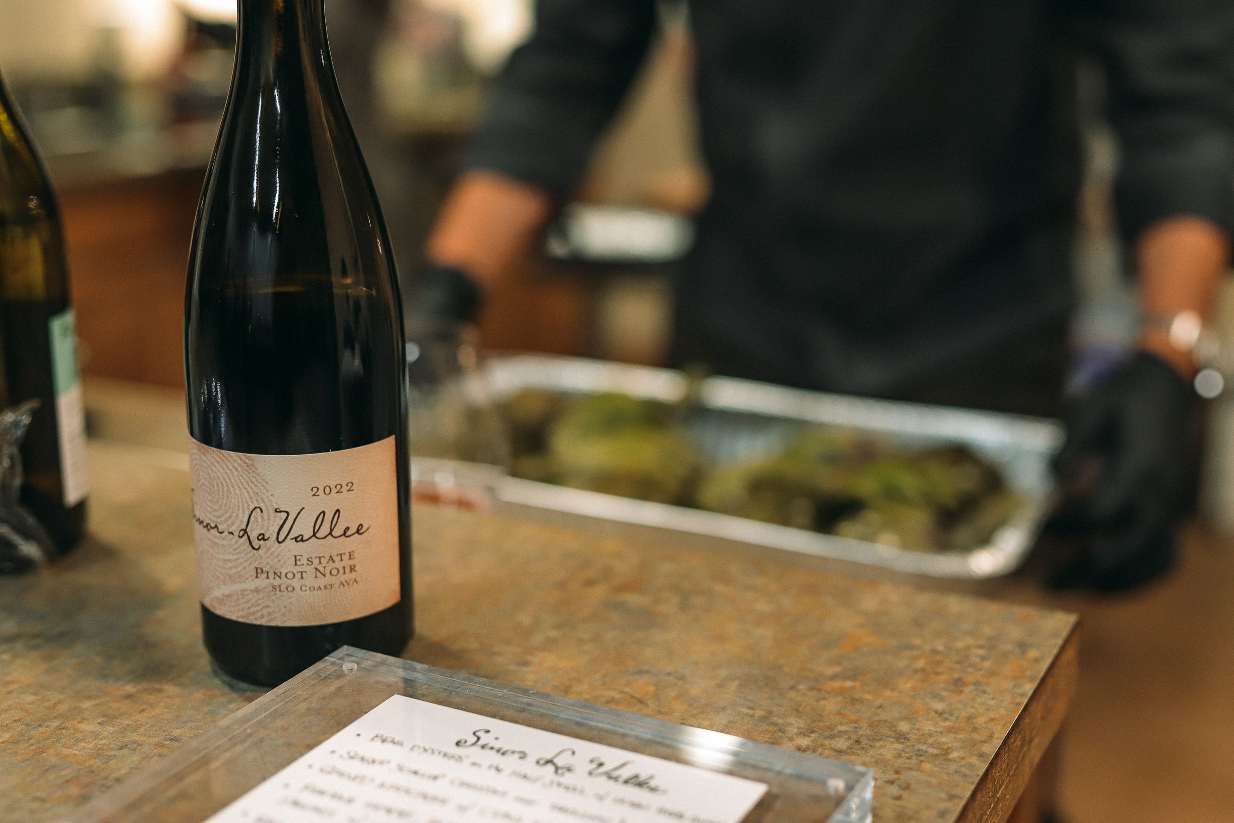 Wine bottle and menu on wooden table in restaurant setting.