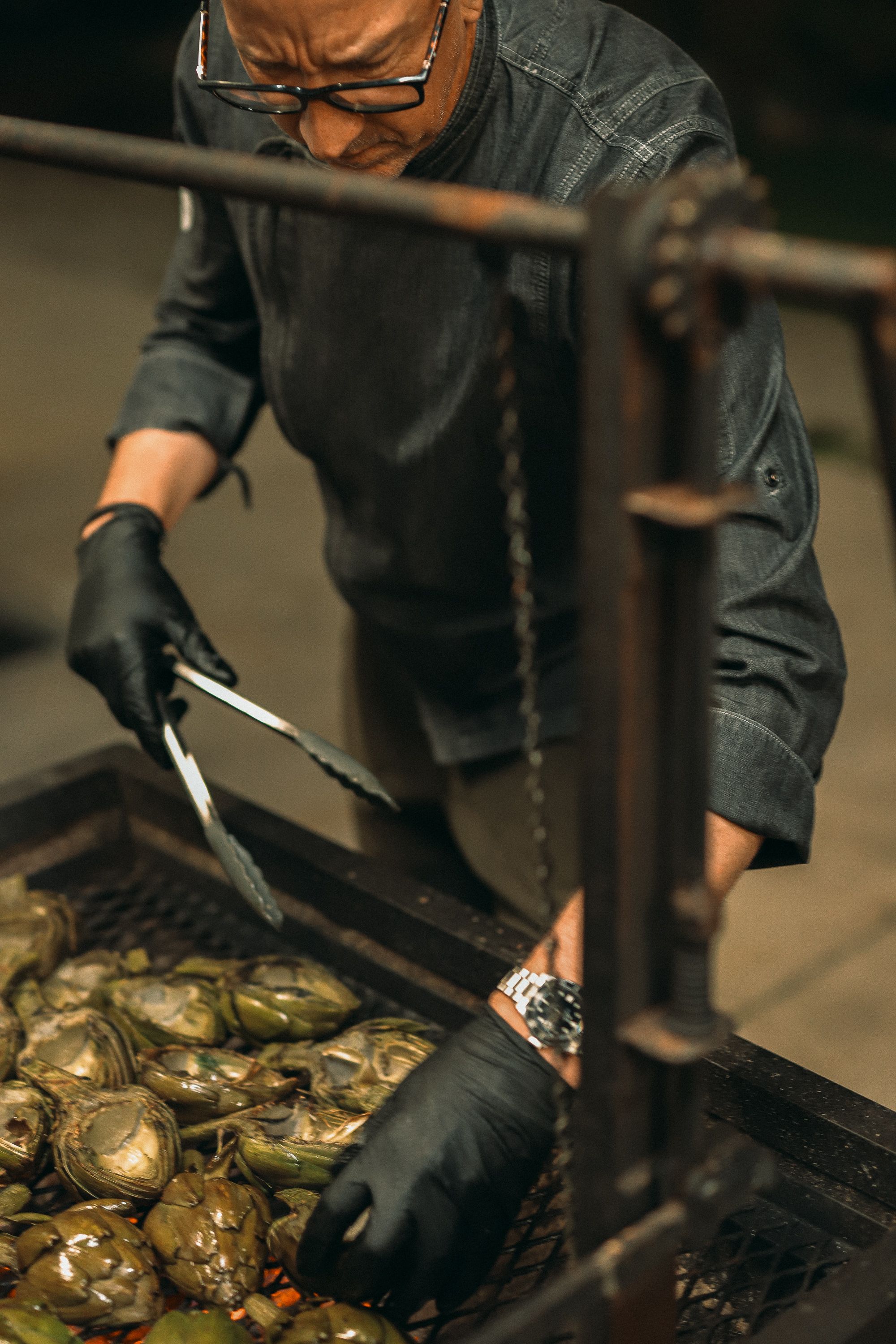 Chef in black gloves shucking fresh oysters at a commercial kitchen station.