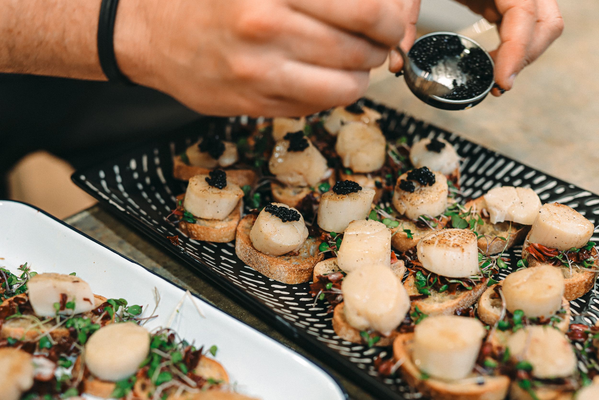 Hands garnishing appetizers on black serving platters.