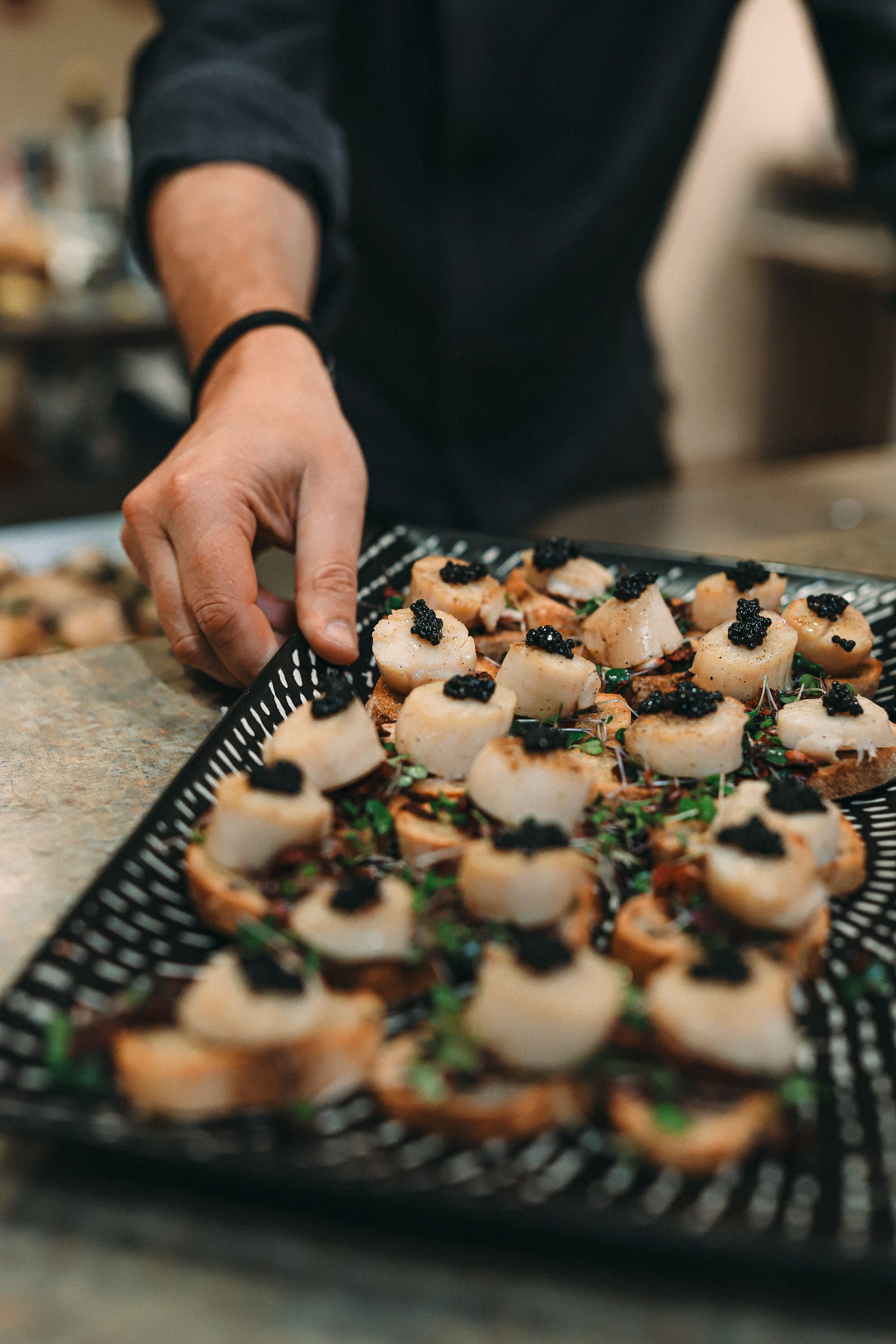 Gourmet appetizers with black caviar and herbs being plated on an elegant black serving tray.