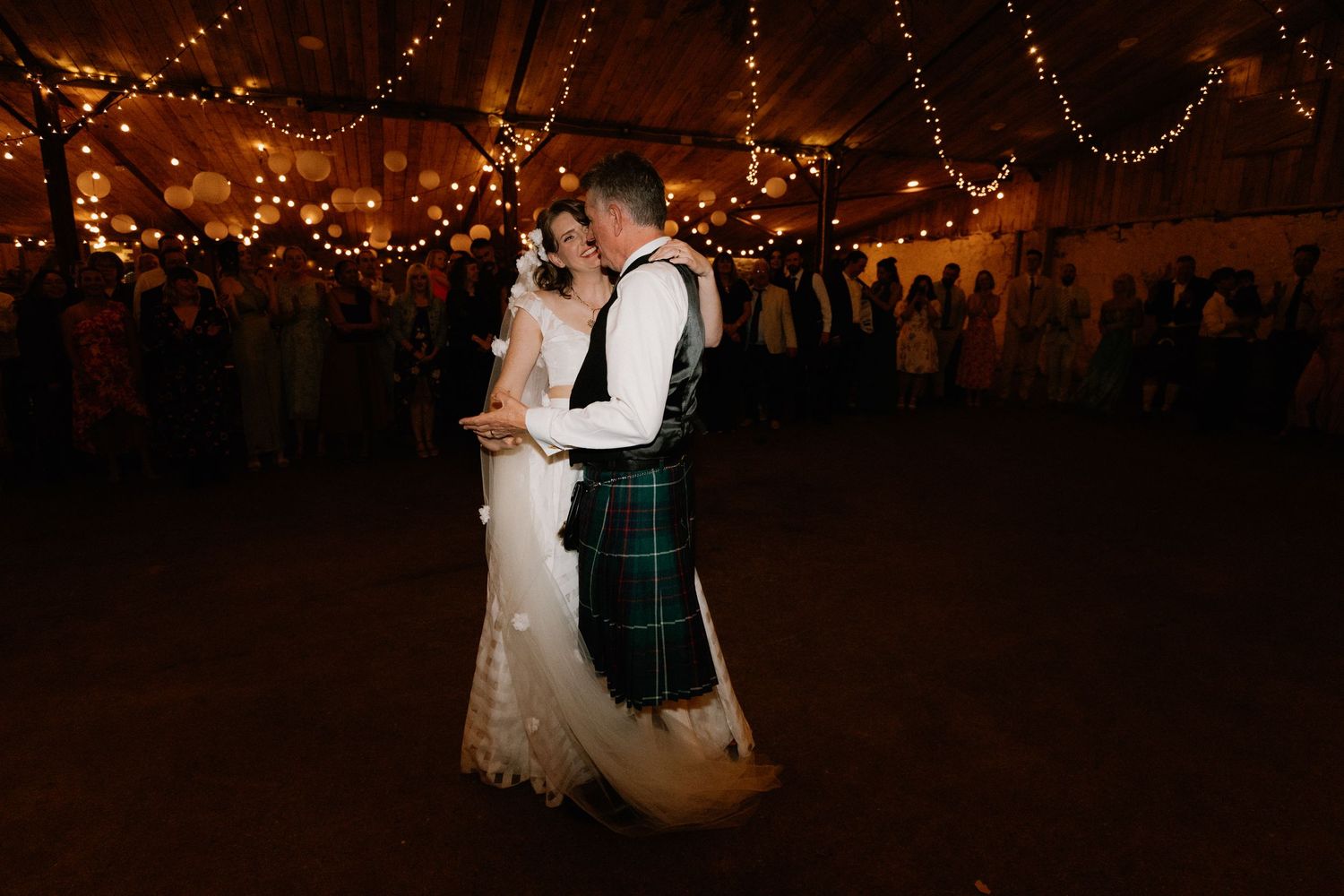 Couple shares romantic dance under twinkling lights at Scottish-themed wedding reception.