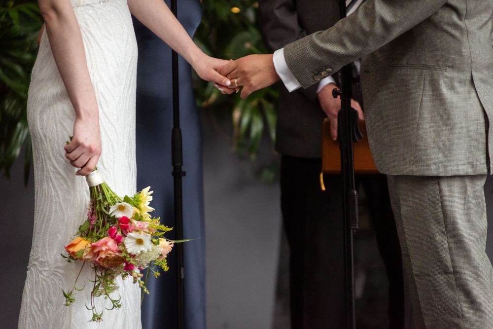 Close-up of joined hands and a bridal bouquet during a wedding ceremony.