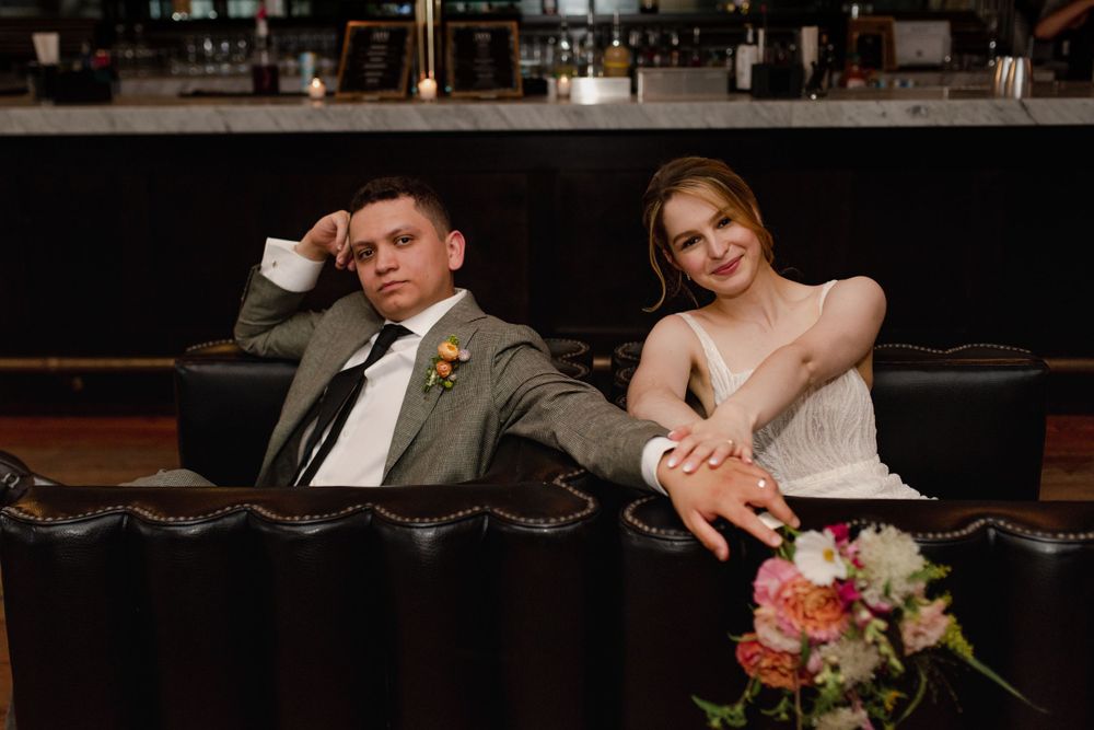 Wedding couple seated together with colorful floral bouquets in an elegant indoor setting.