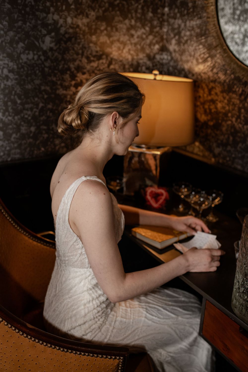 A person in a white wedding dress sits at a desk writing in an intimate, warmly lit room.
