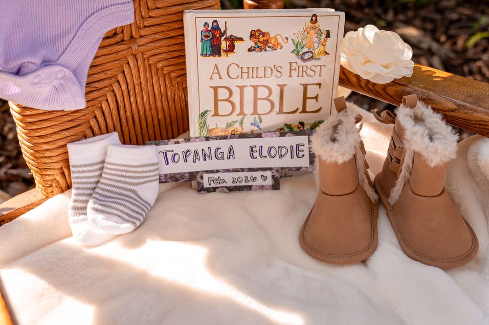 Baby shower gift display with A Child's First Bible, personalized name sign, UGG boots, and striped socks in a wicker basket.