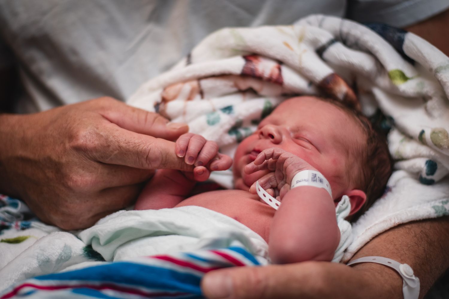 Close-up of newborn baby with hospital bracelet being comforted