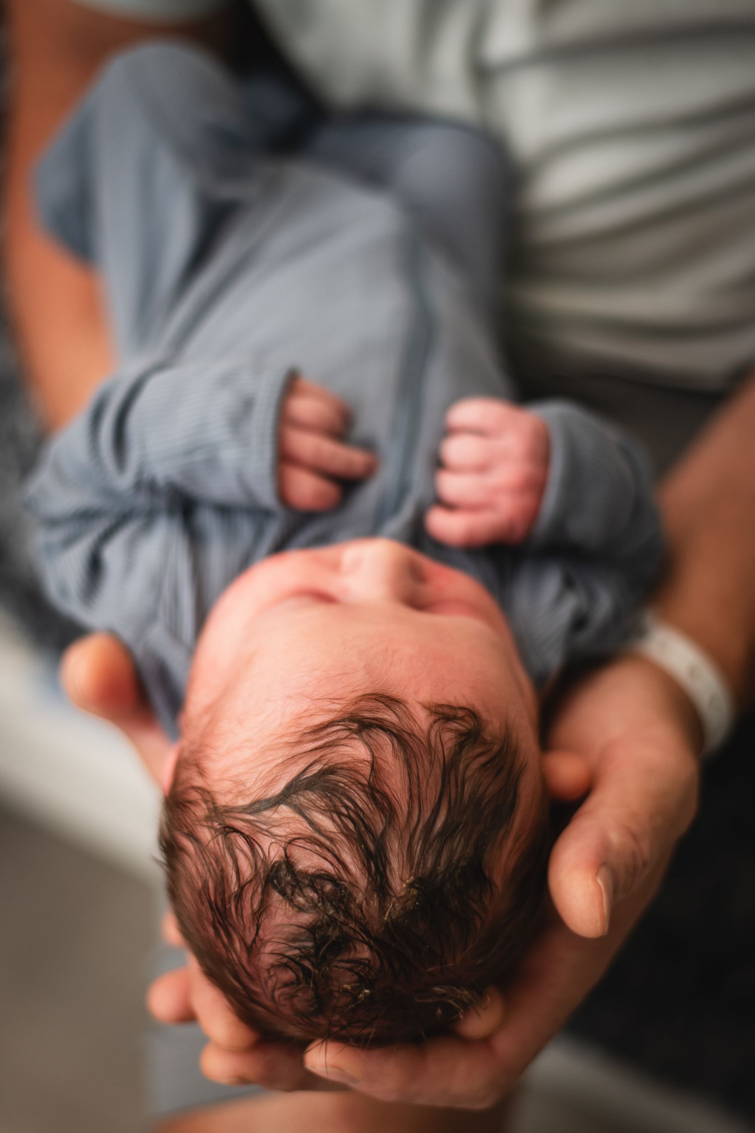 A photo showing a baby's head with dark curly hair being cradled in someone's hands.