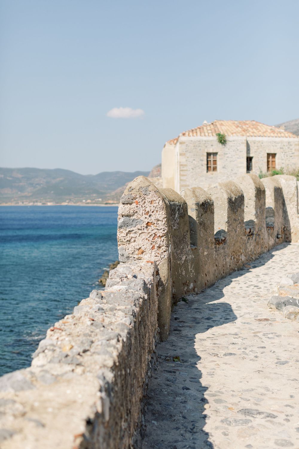 Stone pathway along ancient fortress walls overlooking bright blue Mediterranean waters.