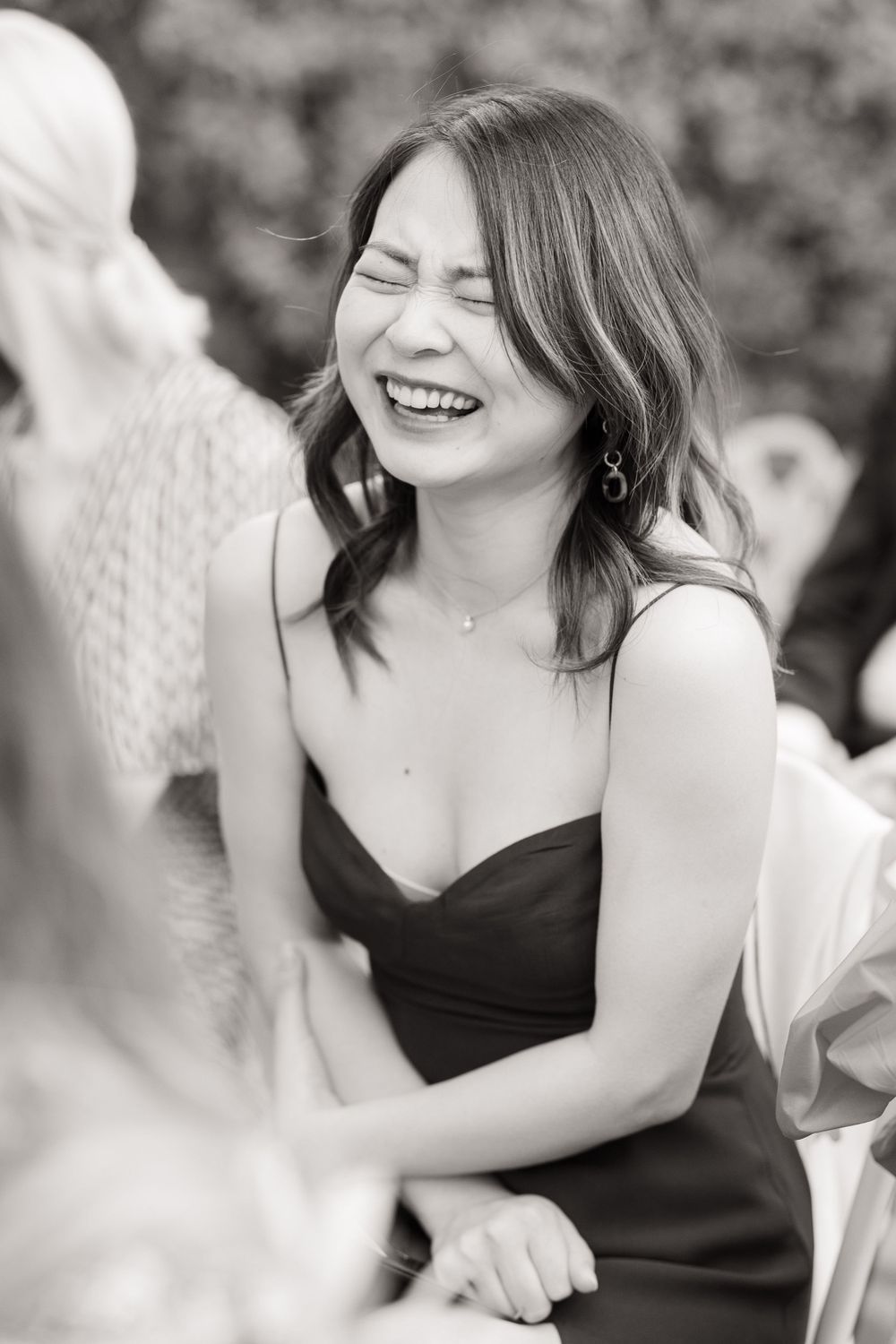 Guest in black dress laughing joyfully during wedding celebration.
