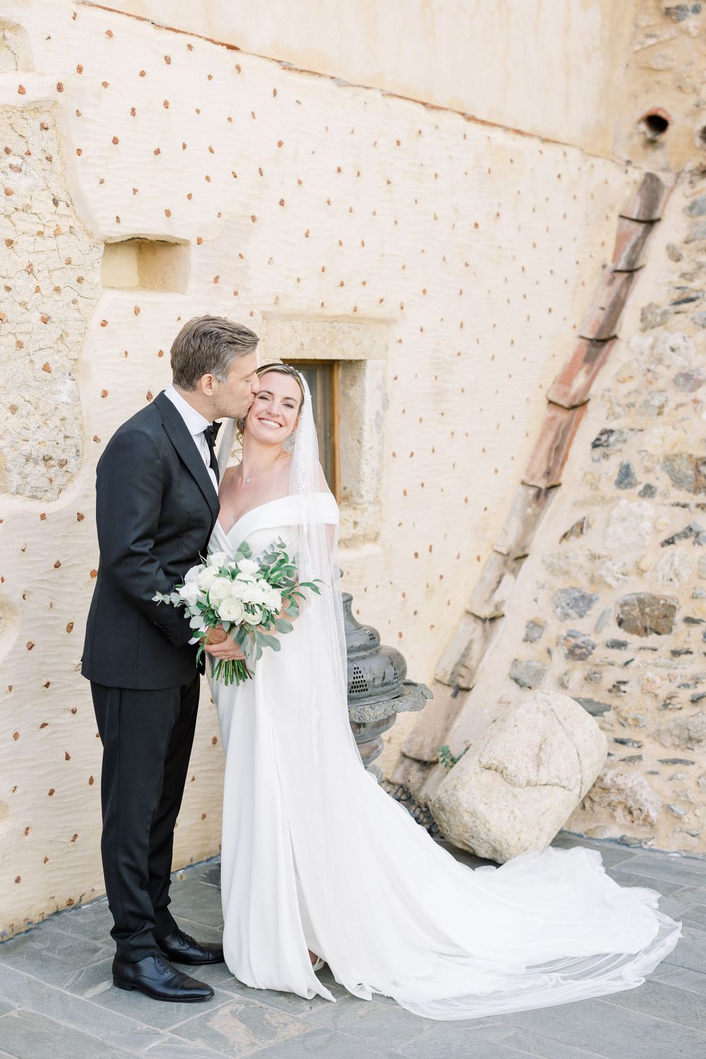 A wedding couple shares an intimate moment against a rustic stone wall backdrop.