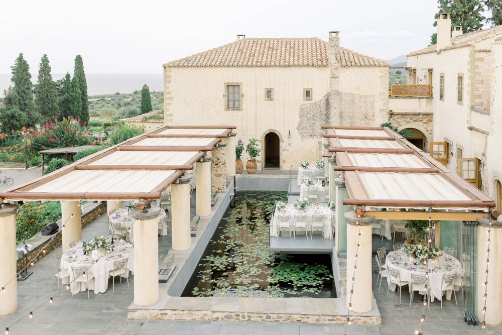 Outdoor wedding reception space with covered walkways and dining tables arranged around a central water feature.