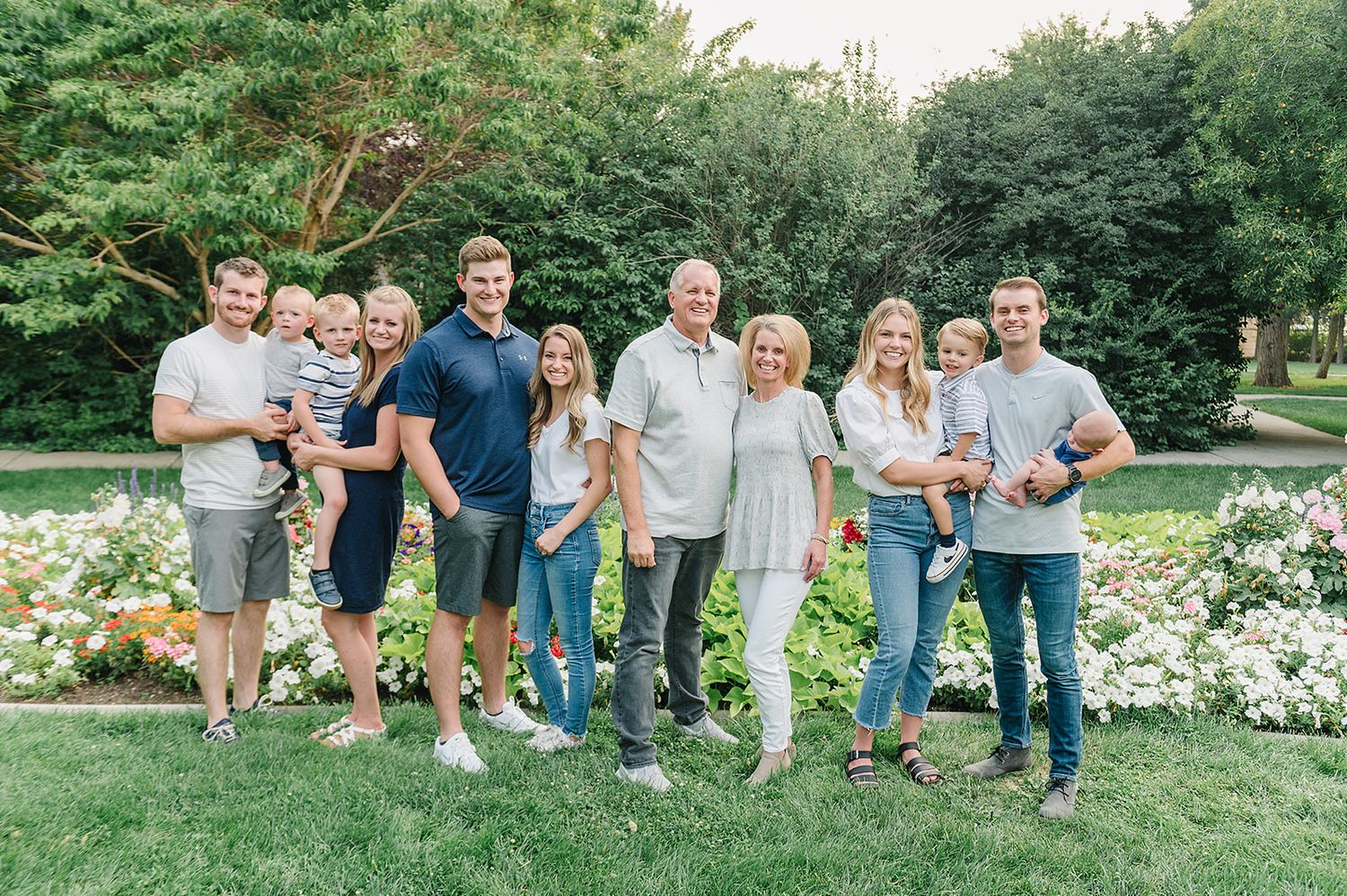 A large family group poses together in front of a blooming garden on a sunny day.