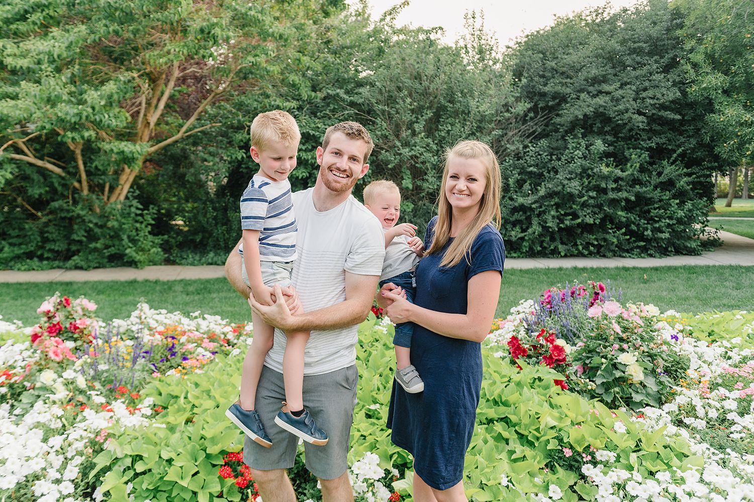 A family poses together in front of a colorful garden filled with blooming flowers.