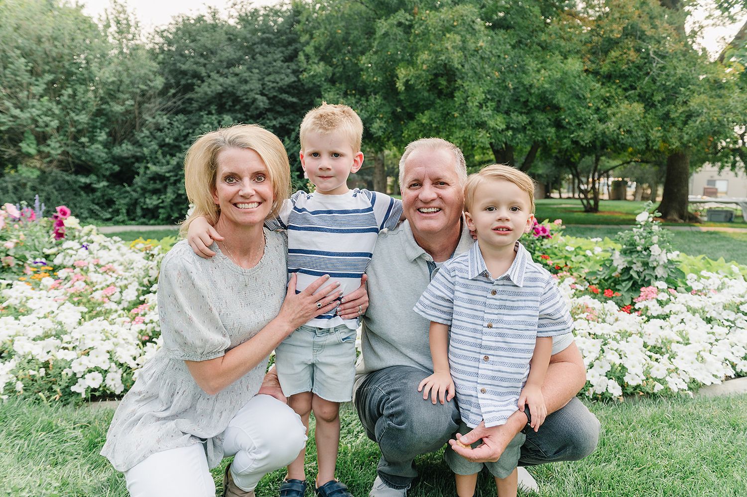 A family group poses together in front of a white flower garden.