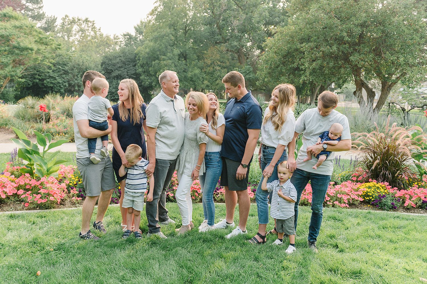 Multiple generations of a family gather together in a lush garden setting with colorful flowers.