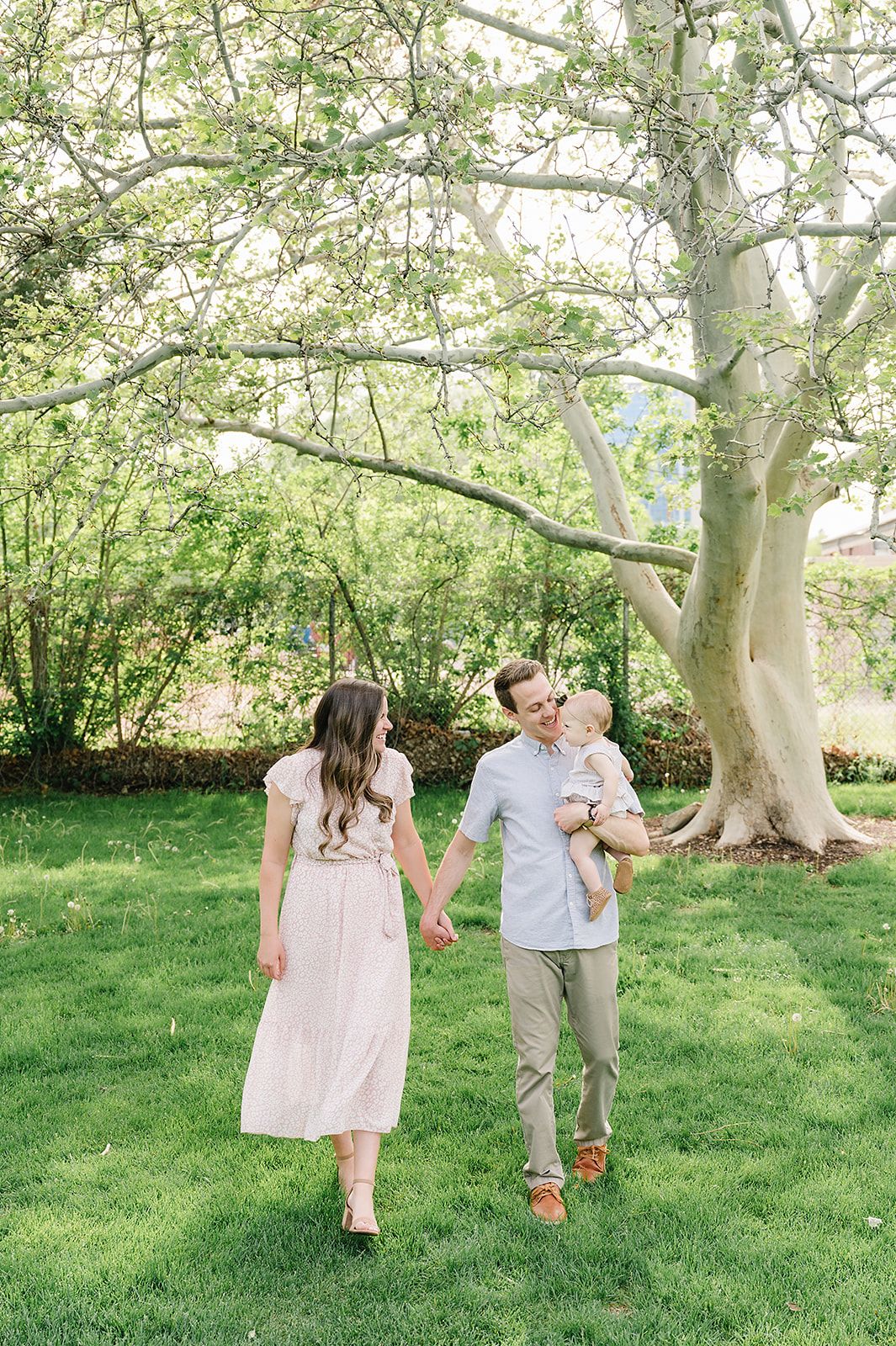 A tender family stroll through a sun-dappled garden with blooming trees overhead.