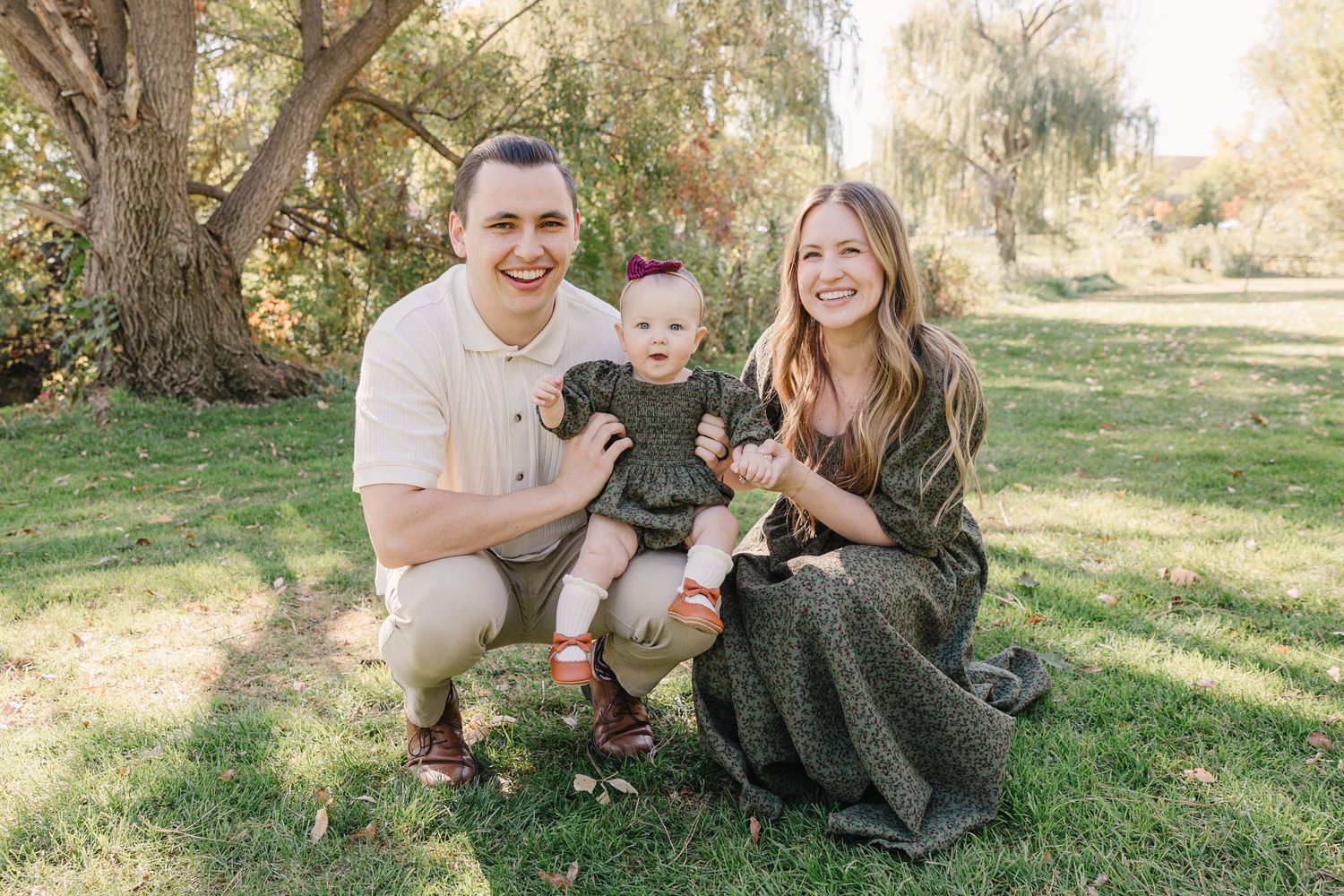 A family sits together on grass beneath autumn trees during a portrait session.