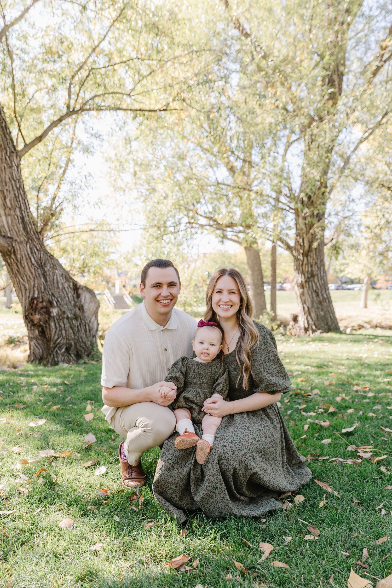 A family portrait taken under golden trees during fall with everyone sitting on green grass.