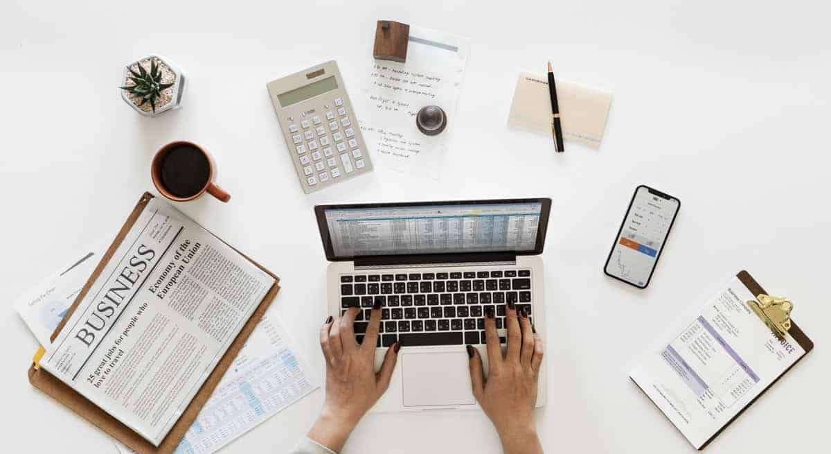 Overhead view of hands typing on laptop surrounded by business documents, calculator, and coffee.