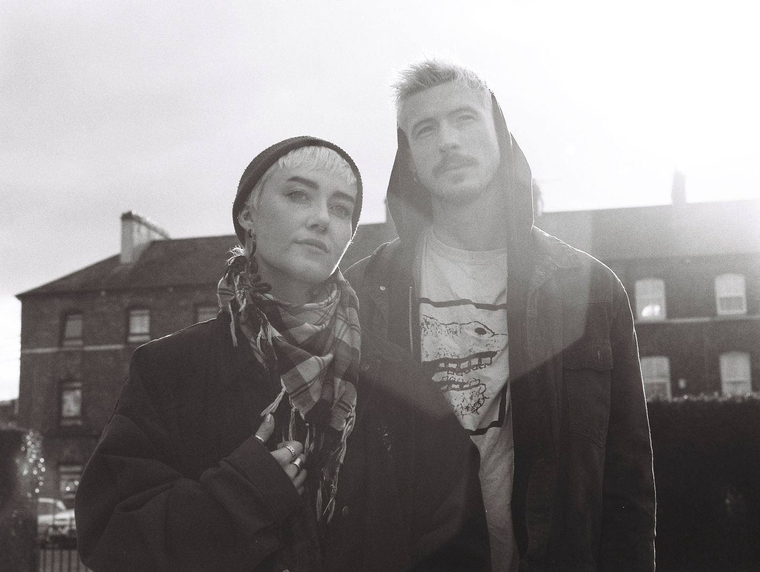 A stylish couple poses together against an urban backdrop in black and white.