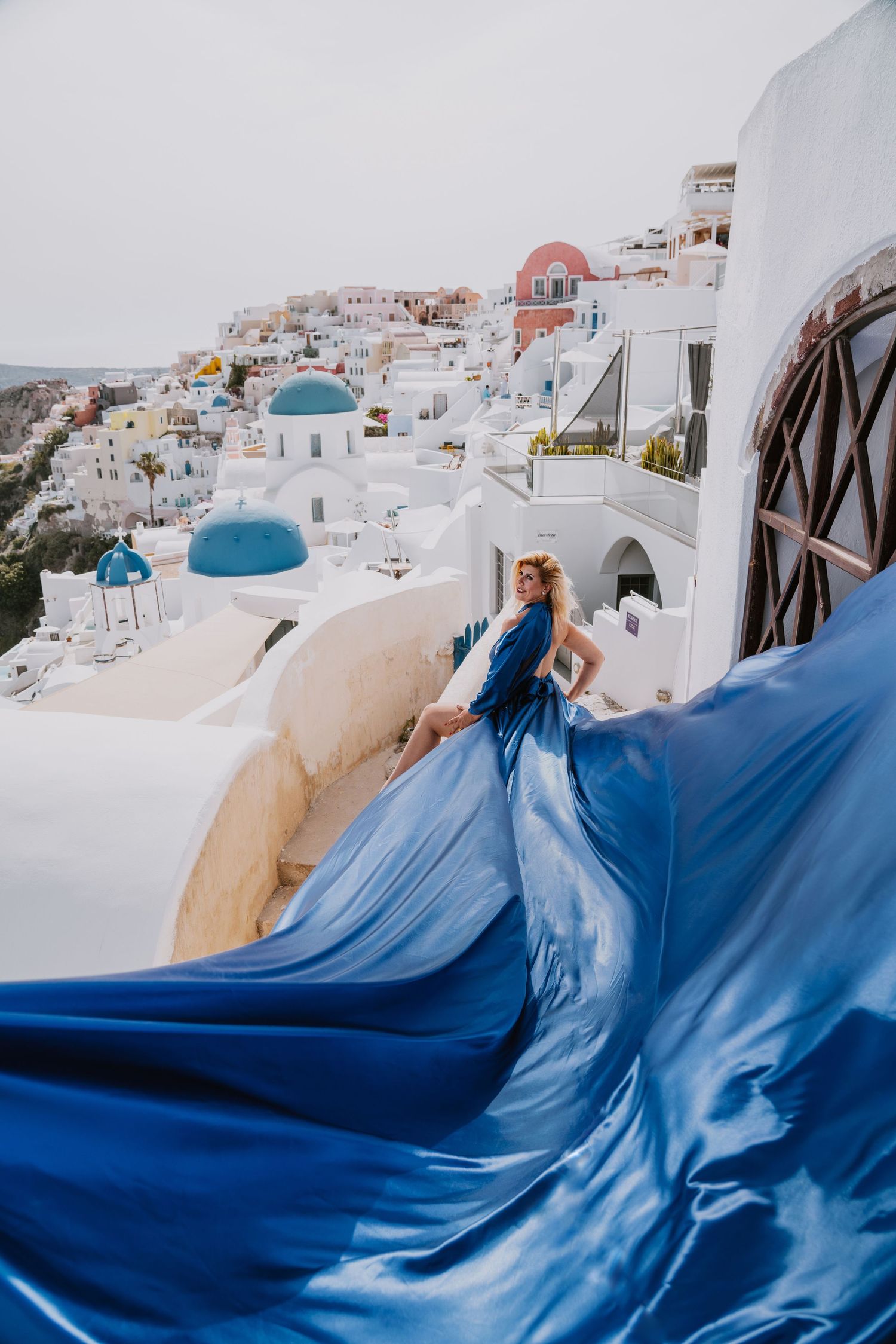 Flowing blue dress against white buildings and blue domes in Santorini, Greece.