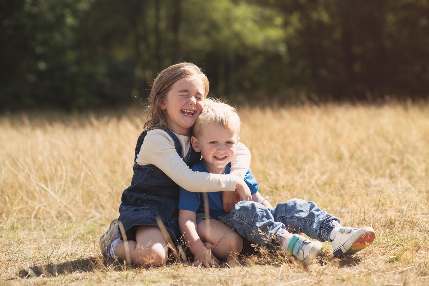 Brother and sister sat in a filed in Summer cuddling and laughing