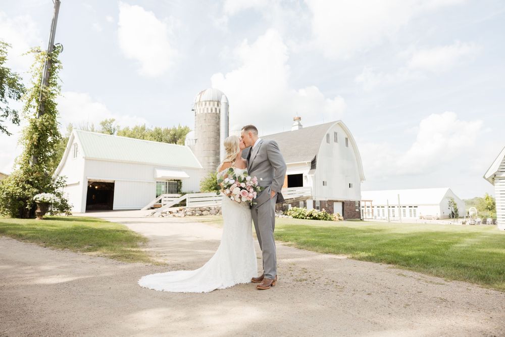 A wedding couple poses for romantic photos in front of a rustic white barn on their special day.