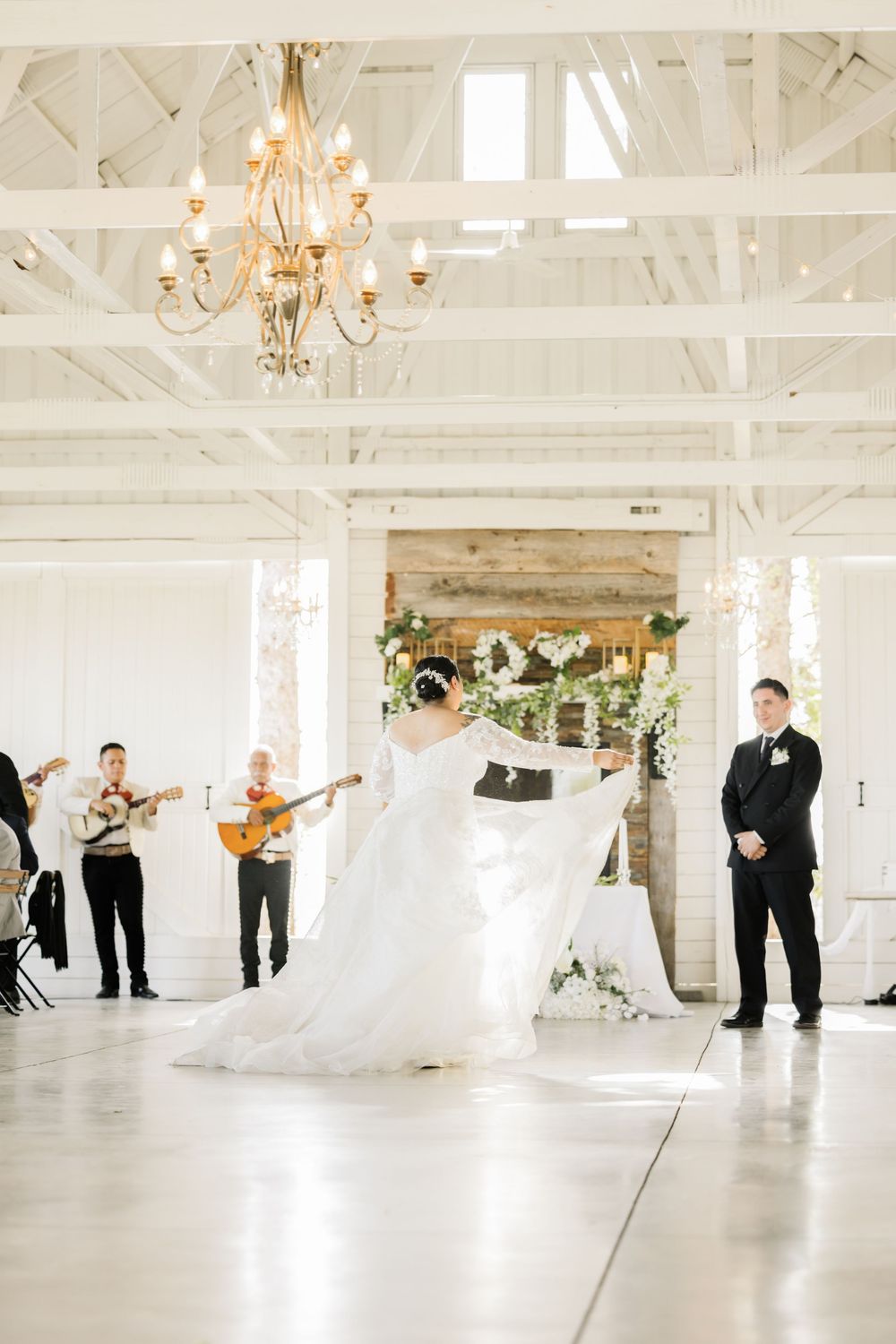 Spacious white reception hall with chandeliers and people dancing in an elegant celebration.