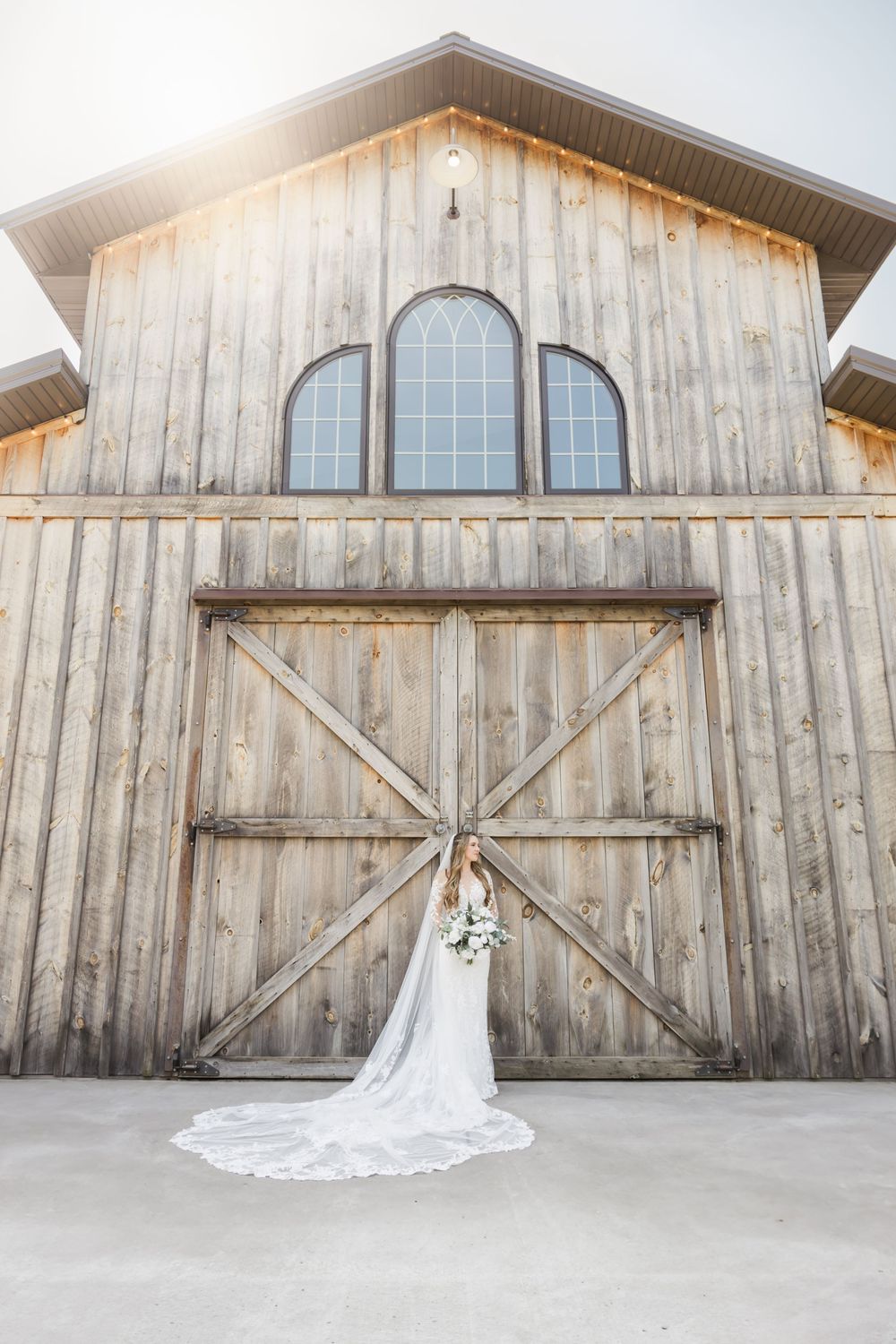 A rustic barn wedding venue with weathered wood siding and a flowing white wedding dress displayed against it.