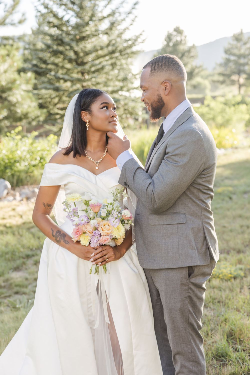 Wedding couple in grey suit and white dress pose together outdoors with a colorful bouquet.