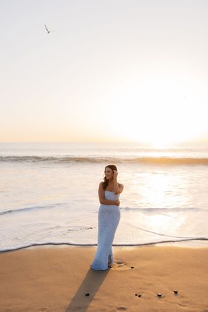 A couple embraces on a sandy beach at sunset with ocean waves rolling in the background.