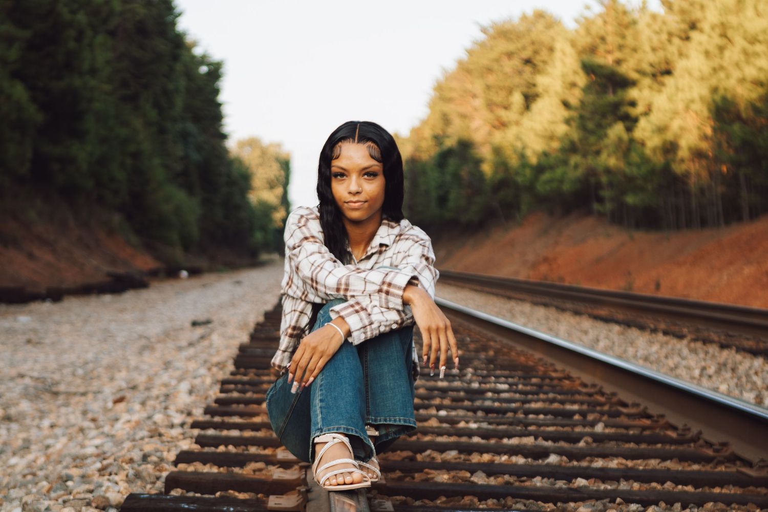 A photoshoot on railroad tracks with a plaid shirt and jeans outfit in golden autumn lighting.