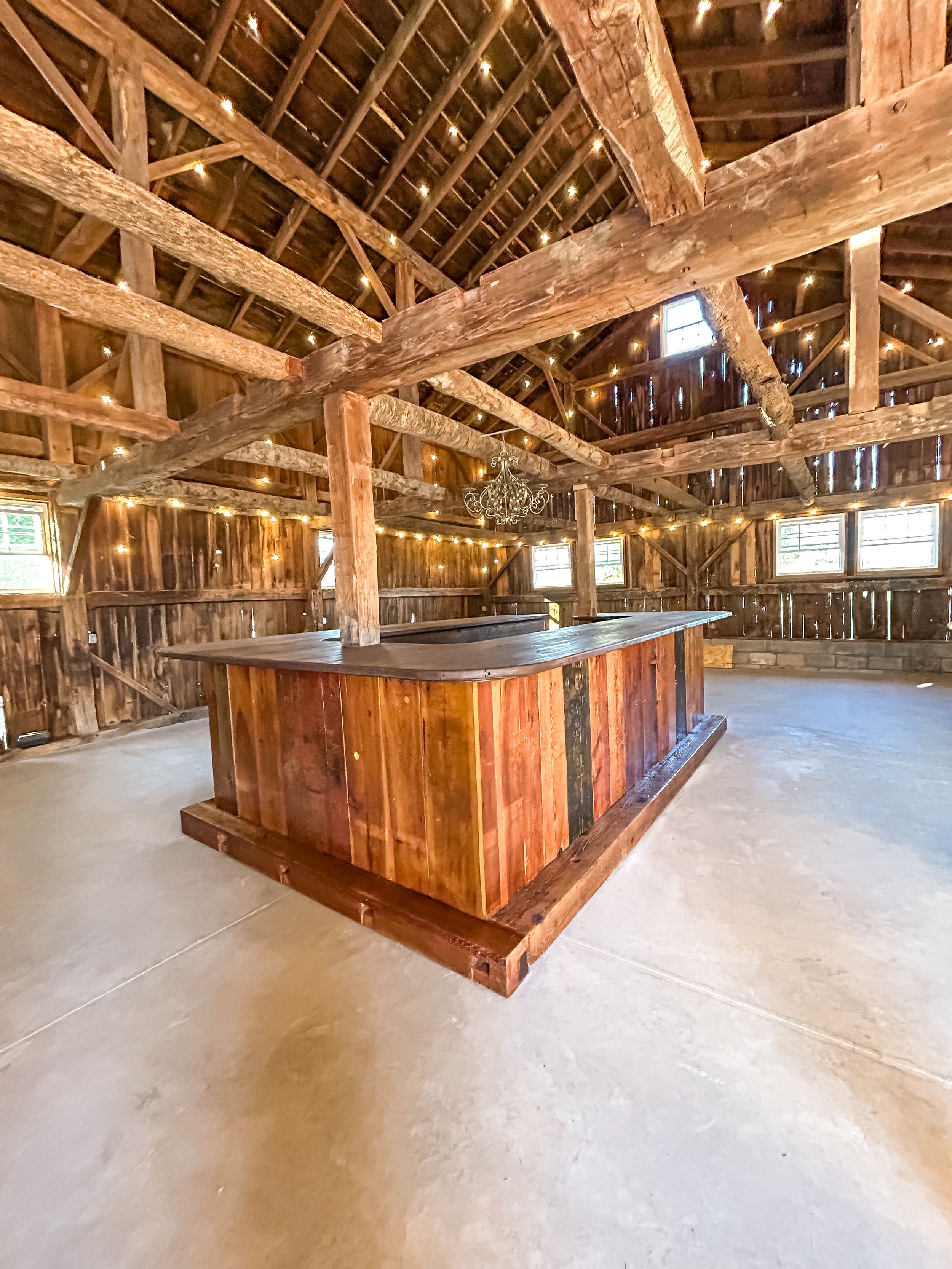 Rustic wooden bar installation inside a restored barn featuring exposed ceiling beams and natural lighting.