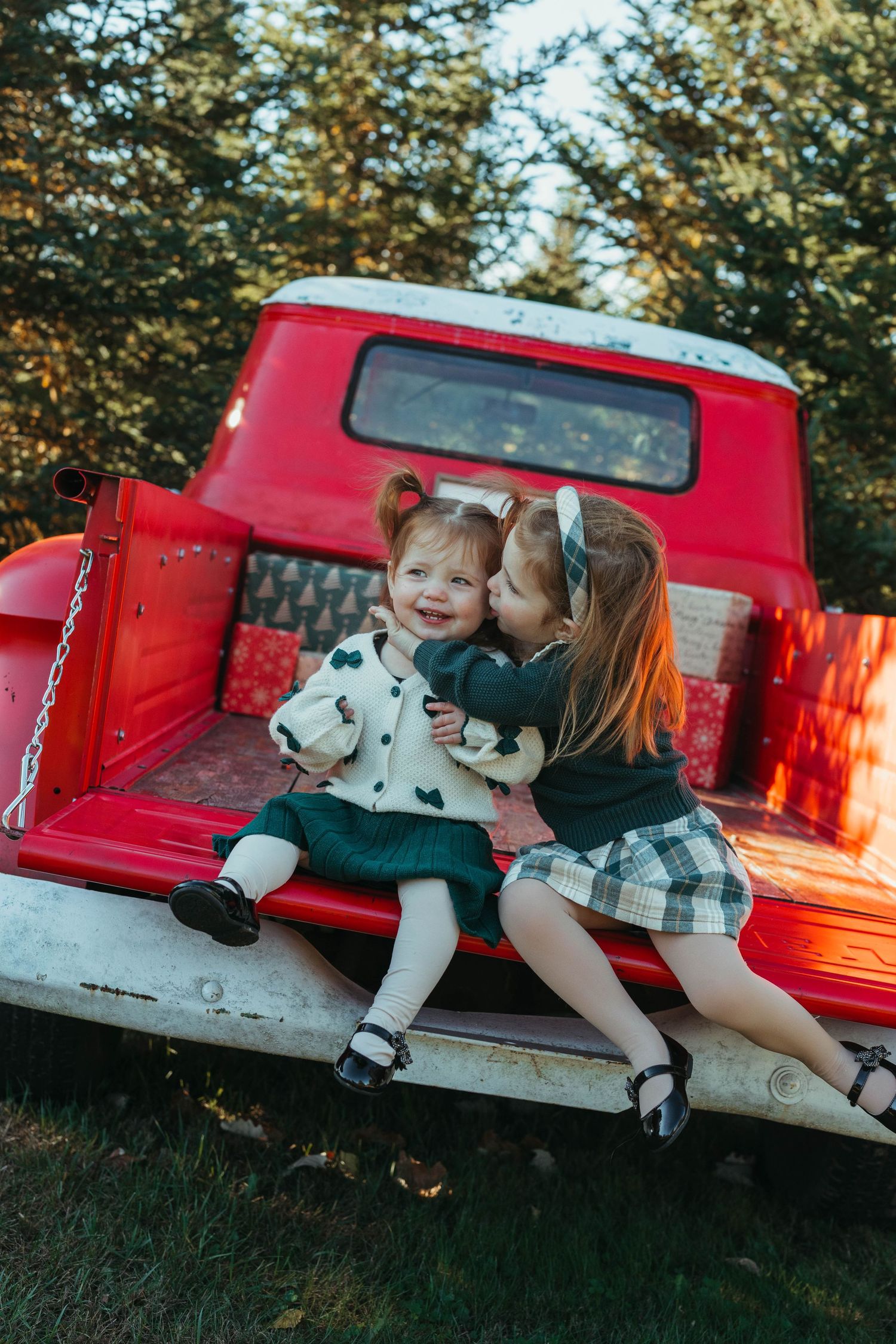 Children play and laugh together on vintage red truck during outdoor photo session.