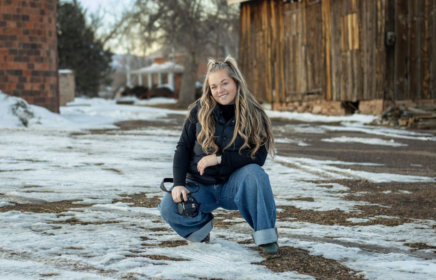 A casual winter portrait in front of rustic wooden buildings with snow on the ground.